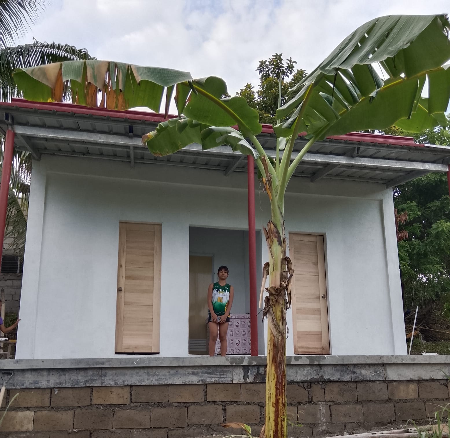 Loyren's daughter standing in the doorway of her family's new white house with a red metal roof